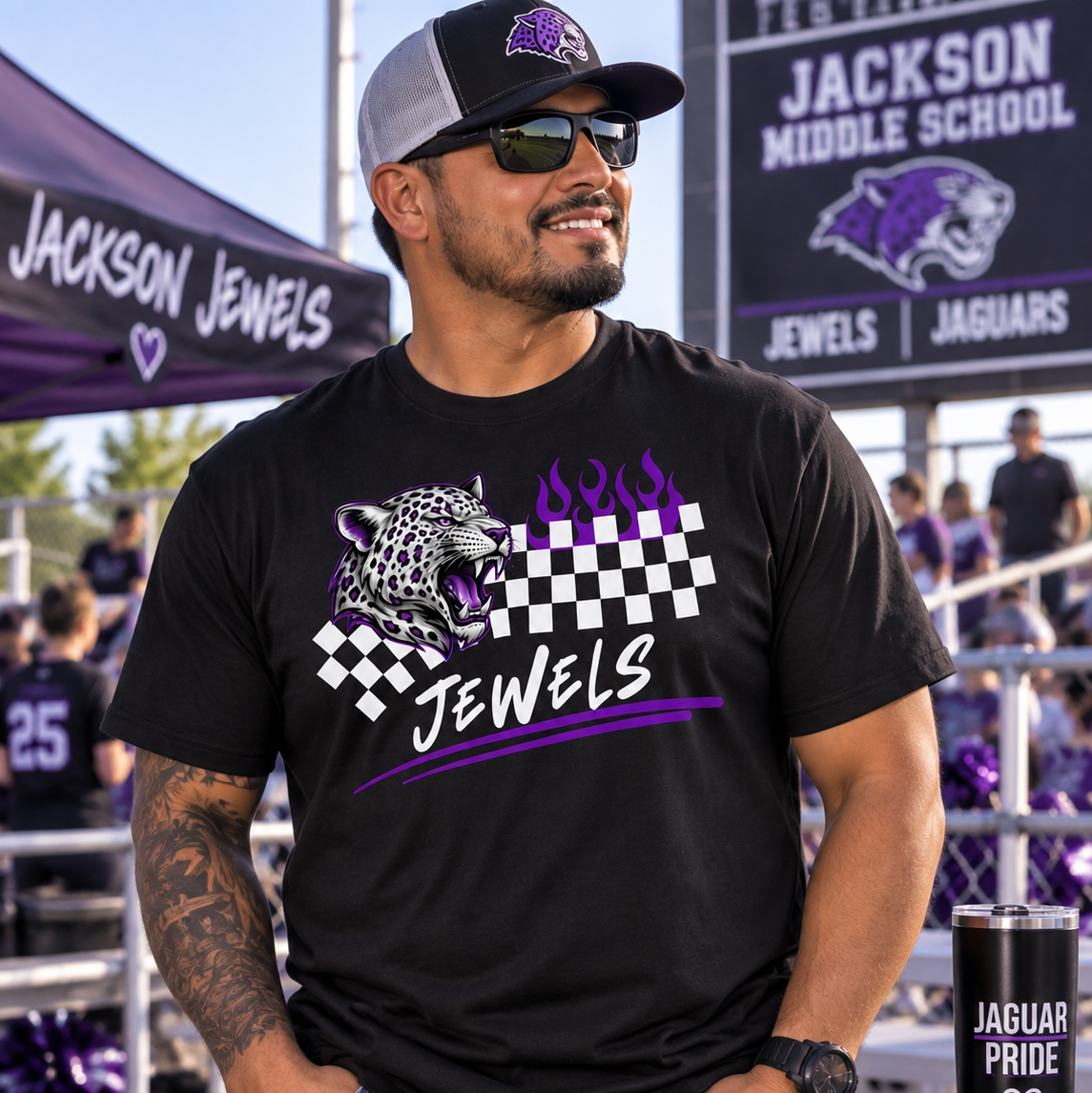 A man wearing a black graphic t-shirt with a purple and white Jaguar design, standing in front of a Jackson Middle School sign. The shirt features a jaguar graphic, a checkered flag, and the word 'JEWELS' in purple and white.
