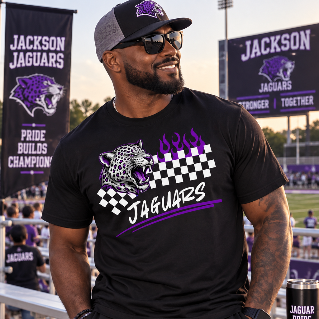 A man wearing a black Jackson Jaguars t-shirt with a purple and white graphic of a jaguar and flames, standing on a sports field with team banners in the background.