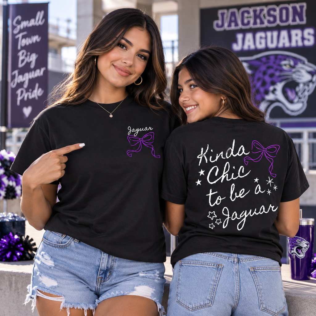 Two women modeling black graphic t-shirts with purple and white designs. The front shirt features 'Jaguar' text with a purple ribbon, and the back shirt reads 'Kinda Chic to be a Jaguar' with white script and stars.