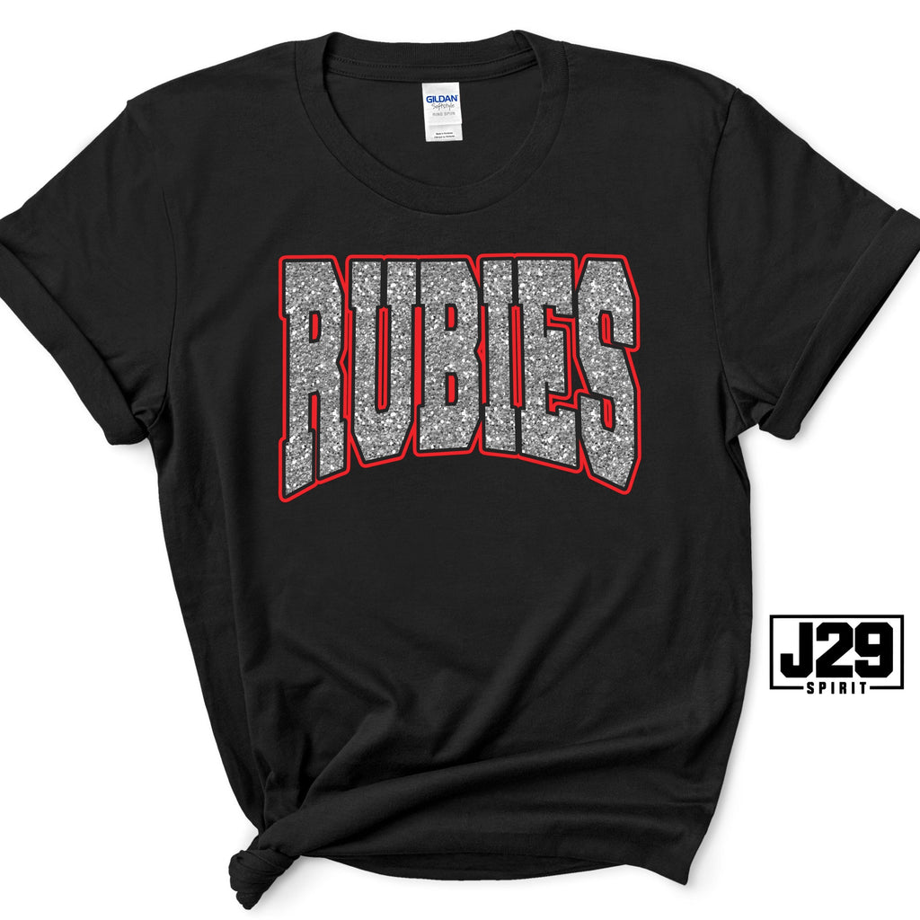 A black short-sleeve t-shirt with a graphic reading 'RUBIES' in silver glitter-style letters with a red outline, displayed on a white background with a J29 Spirit logo overlay.