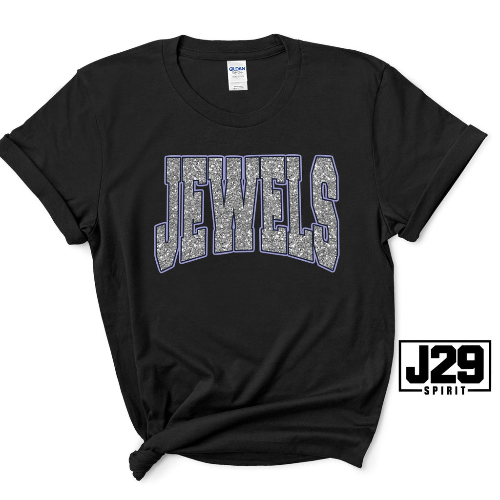 A black short-sleeve t-shirt with 'JEWELS' printed across the chest in a gray and white textured pattern with a blue outline. The shirt is styled with a knot at the bottom hem and features a 'J29 SPIRIT' logo overlay in the bottom right corner.