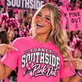 A woman in a bright pink cheerleader outfit and hair bow points to a matching pink graphic t-shirt that reads 'FORNEY SOUTHSIDE Pink Out' with a pink ribbon. The background shows a crowded gymnasium with pink signs and cheerleaders.